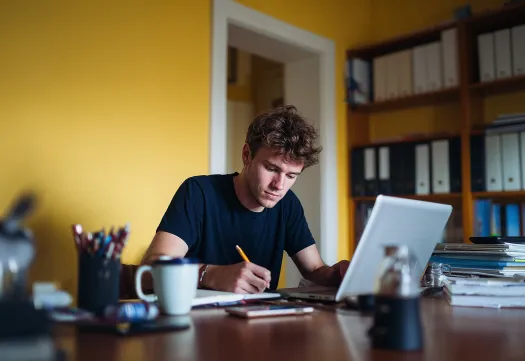 Un étudiant étudie à son bureau avec un ordinateur portable et des documents. 