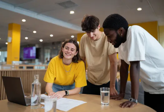 Trois étudiants travaillent ensemble autour d’une table avec un ordinateur portable. 